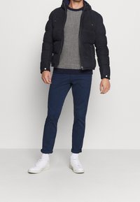 Námořnicky modrá péřová bunda s kapucí, texturovaný šedý pletený svetr, námořnicky modré kalhoty a bílé tenisky. Minimalistický design se zipy a knoflíkovými detaily.