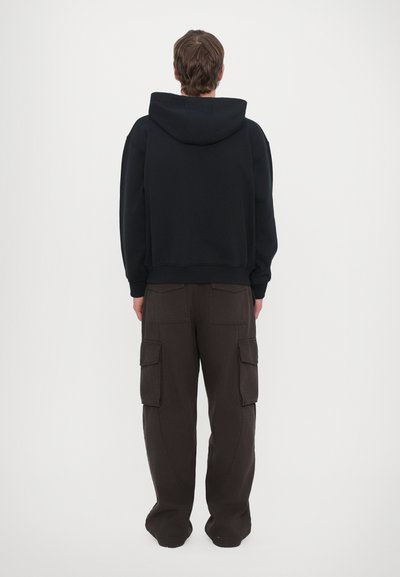 Felpa nera con cappuccio in morbido tessuto, abbinata a pantaloni cargo larghi di colore marrone scuro con numerose tasche.