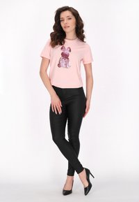 Růžové tričko s krátkým rukávem s designem králíka vyrobeným z růžových a stříbrných flitrů; doplněné o černé fitted kalhoty a černé podpatky.