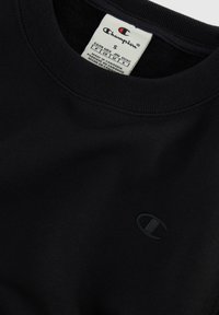 Sudadera de algodón negra con cuello redondo. Presenta un sutil logo bordado en el pecho. Tejido suave y texturizado, talla pequeña.