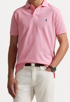 Koszulka polo z jasnoróżnęj bawełny z dwoma guzikami, krótkimi rękawami i haftowanym logo na piersi, w połączeniu z białymi spodniami.