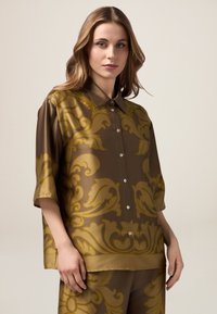 Chemise courte en satin marron à manches courtes, ornée d'un motif baroque doré, avec des boutons sur le devant et une coupe décontractée au toucher doux.