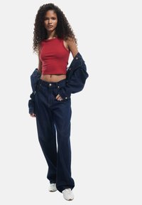 Punainen ribbitekstuuri crop-top yhdistettynä tummansinisiin hyvän kokoisiin farkkuihin. Asu sisältää farkkutakin heitettynä hartioille ja valkoiset tennarit.