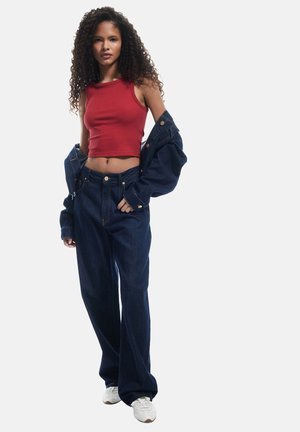 Rood geribbelde crop top gecombineerd met donkerblauwe, losse spijkerbroeken. De outfit bevat een spijkerjack dat over de schouders hangt en witte sneakers.