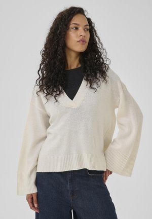 Ecrufarbener Oversize-Pullover mit V-Ausschnitt und weiten Ärmeln, ausgestattet mit gerippten Bündchen und Saum, aus einem weichen, strukturierten Stoff gefertigt.