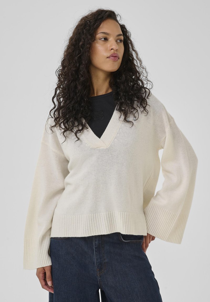 Pull oversized couleur crème avec un décolleté en V et des manches larges, doté de poignets et d'un ourlet côtelés, fabriqué à partir d'un tissu doux et texturé.