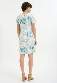 Kwiatowa sukienka w białym kolorze z niebieskimi i zielonymi wzorami, z krótkimi rękawami i dekoltem w kształcie łezki. Połączona z beżowymi sandałami na słupku.