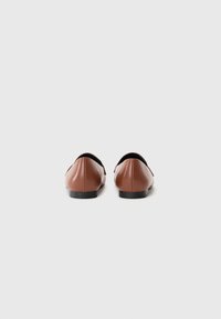 Ballerines en cuir marron avec un bout arrondi et une semelle noire basse. L'arrière a une finition lisse sans quincaillerie visible ni embellissements.