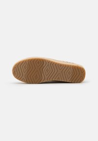 Shoe outsole with a textured rubber surface, featuring a zigzag pattern and logo. Color is light brown with a smooth finish.