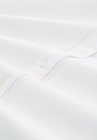 Camicia bianca in cotone con una consistenza liscia, numerosi bottoni con una lucentezza sottile e dettagli di cucitura precisi.