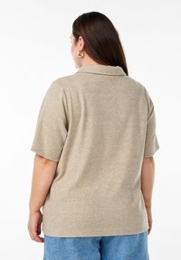 Polo beige a maniche corte con colletto, realizzato in tessuto a maglia testurizzata. Il retro è semplice, con una vestibilità rilassata, abbinato a pantaloncini in denim.