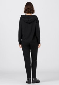 Černá mikina s kapucí a odpovídající kalhoty, které mají volný střih, měkkou látku a nastavitelnou kapuci. Nošeno s černými kotníkovými botami.