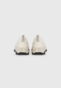 Light beige trail shoes with textured mesh upper, geometric-shaped light gray midsole, and black rubber outsole featuring prominent studs.