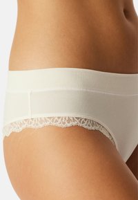 Culottes en coton couleur crème avec une taille élastique blanche et une délicate bordure en dentelle, présentant une texture lisse et une coupe ajustée.