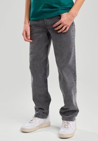 Pantalones de denim gris con corte relajado y pierna recta, combinados con zapatillas blancas. Textura suave y detalles de costura mínimos.