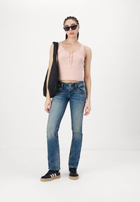 Pink ribbed crop top with front button detail, paired with faded blue straight-leg jeans and black sneakers with white stripes. Black tote bag.