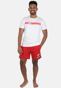 Hvid t-shirt med røde vandrette striber og teksten "VIVID", parret med røde badebukser med palmetrædesign og logo.
