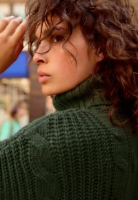 Strik en grøn turtleneck sweater med teksturerede mønstre og en tyk vævning, med et nærbillede af halsudskæringen og skulderområdet.