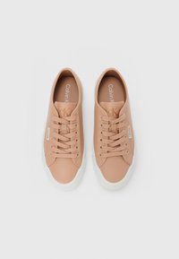 Pair of beige Calvin Klein low-top sneakers with laces and white rubber soles, viewed from above on white background.