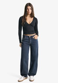 Černý top s dlouhým rukávem a véčkovým výstřihem, kombinovaný s volnými tmavě modrými džíny. Boty jsou bílé s světle hnědými akcenty. Jednoduchý a přiléhavý design.