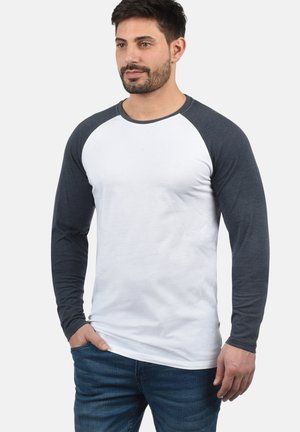 Long-sleeve raglan t-shirt featuring white body and dark gray sleeves, made of soft cotton with a smooth texture and contrasting neckline.