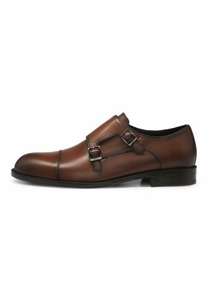 Chaussure habillée à double boucle en cuir marron avec semelle en caoutchouc noire, bout arrondi et boucles argentées sur le côté.