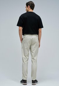 T-shirt noir à manches courtes associé à un pantalon beige clair. Le pantalon présente une coupe décontractée et une taille élastique, avec deux poches arrière.