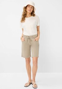 Shorts beiges avec une taille à cordon et des poches avant, associés à un t-shirt de couleur claire et un chapeau de pêcheur, complétés par des sandales.