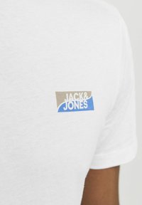 Hvid bomuld t-shirt med et flerfarvet logo i beige og blå, der står "JACK & JONES" på den øverste del af ryggen. Korte ærmer.