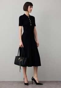 Must ribiga kleit lühikeste varrukatega ja nööpdetailidega, volditud seelik, koos musta käekoti ja teravate varbaga kontsakingadega. Sile tekstuur.