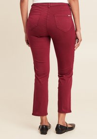 Bordeaux stretchbroek met een getailleerd ontwerp, middelhoge taille en achterzakken. Soepele textuur en lichte flare aan de zoom.