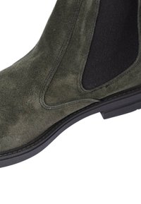 Stivale alla caviglia verde in suede con pannelli laterali elasticizzati, punta rotonda e suola in gomma, con cuciture visibili lungo i bordi.