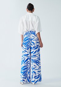 Chemise blanche avec un empiècement au dos, associée à un pantalon large taille haute en motif animal bleu et blanc. Texture lisse.