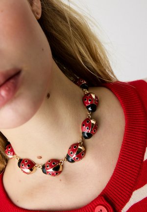Halskæde med store røde og sorte perler formet som mariehøns, båret over en rød sweater med hvide striber.
