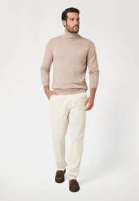 Maglione beige a collo alto con dettagli a coste, abbinato a pantaloni color crema e mocassini marroni. Texture liscia, design aderente e colori neutri.