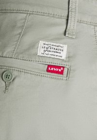 Light green cotton pants with a button closure, featuring a white label "LEVI STRAUSS of CALIFORNIA" and a red "LEVI'S®" tag on the pocket.