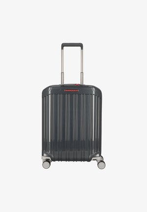 Valise rigide gris foncé avec des rainures verticales, poignée rétractable extensible, quatre roues pivotantes et accent logo rouge.