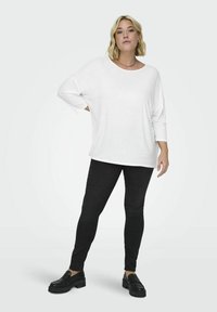 Top blanco de gran tamaño y de manga larga combinado con pantalones ajustados negros y zapatos de plataforma negros. Diseño sencillo con un ajuste relajado.