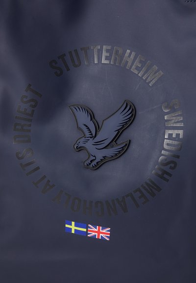 Mørkeblå vanntett veske med et fremtredende ørneemblem og preget tekst. Inkluderer svenske og britiske flagg-lapper på bunnen.