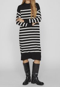 Svart och vit randig stickad klänning med långa ärmar och rundad halsringning, tillsammans med knähöga svarta läderstövlar.