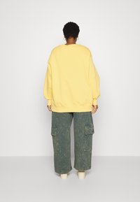 Överdimensionerad gul sweatshirt med sänkta axlar, ribbade ärmmuddar och nederkant, tillsammans med lösa, cargo-stil gröna byxor som har sidofickor.