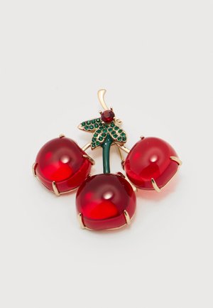 Brooch shaped like three red jeweled cherries with gold-tone stems and green gem-embellished leaves on a white background.