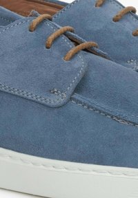 Blauwe suède schoenen met brown textiele veters, een platte zool en stikselafwerking langs de randen. Het ontwerp is minimalistisch en soepel.