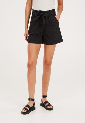 Zwarte katoenen shorts met een hoge taille, een strik aan de voorkant en zijzakken. Gecombineerd met zwarte sandaaltjes met bandjes en een gesp.