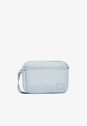 Světle modrá obdélníková crossbody taška Reebok s přední kapsou na zip a nastavitelným šedým popruhem na bílém pozadí.