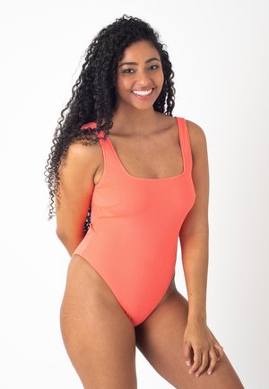 Maillot de bain une pièce en corail avec un décolleté carré et des bretelles larges. Texture lisse, jambes hautes et design minimaliste.