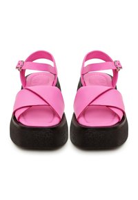 Sandales à plateforme roses avec des sangles entrecroisées, des boucles réglables et une semelle noire texturée, fabriquées en matériau synthétique lisse.