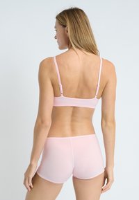 Set di bralette e boyshort rosa chiaro, caratterizzato da spalline regolabili e una texture liscia. Design minimalista senza motivi o parti metalliche visibili.