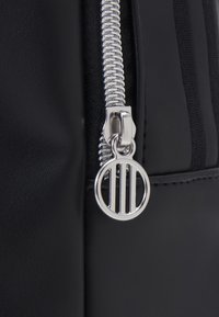 Black leather bag featuring a silver zipper and circular pull tab with a striped cutout design. Smooth texture and minimal accents.