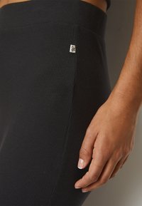 Zwarte geribde legging met een tailleband die is voorzien van een klein logo-label. De stof lijkt zacht met een gladde textuur en een figuuraccentuerend ontwerp.